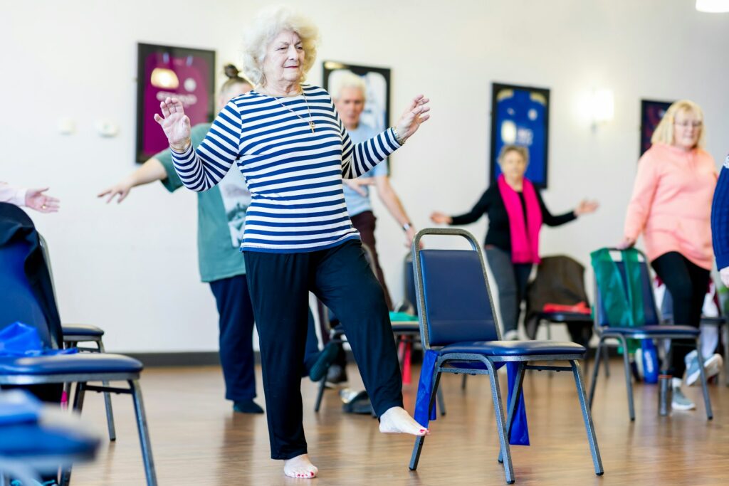 Cours de gym douce pour seniors : une femme âgée fait un exercice d'équilibre parmi un groupe en salle